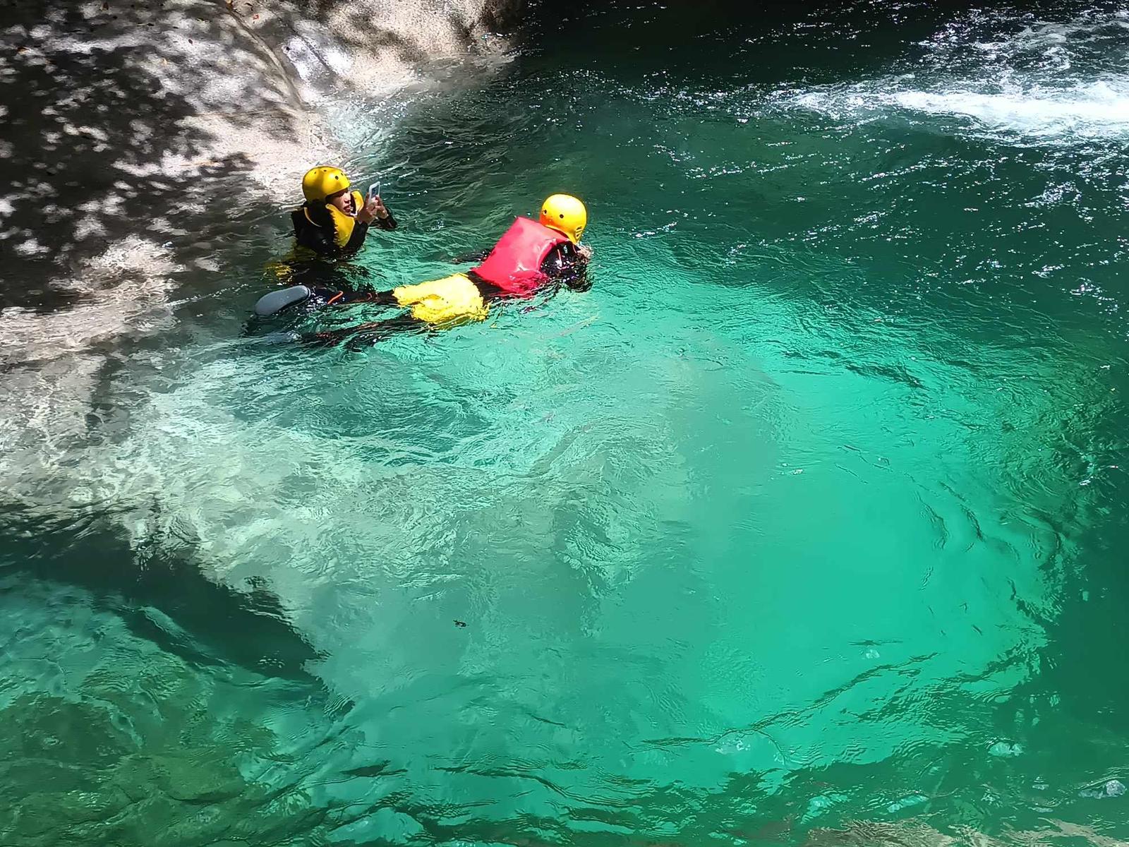 ヘルメットとライフジャケットを着けて、透き通った水色の淵に浮かぶ二人